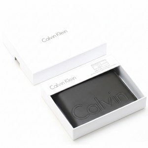 A Calvin Klein men's black leather wallet with debossed Calvin lettering, elegantly presented inside an open white branded gift box
