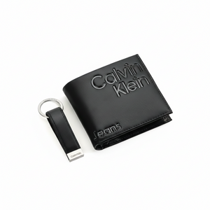 Top-down view of a premium Calvin Klein Jeans men's gift set featuring a black smooth leather bifold wallet with bold embossed branding and a matching leather keychain