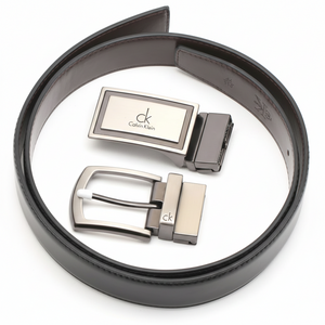 Top-down view of a Calvin Klein men's reversible leather belt set in black, featuring two premium interchangeable metal buckles: a sleek modern plaque and a classic pin buckle