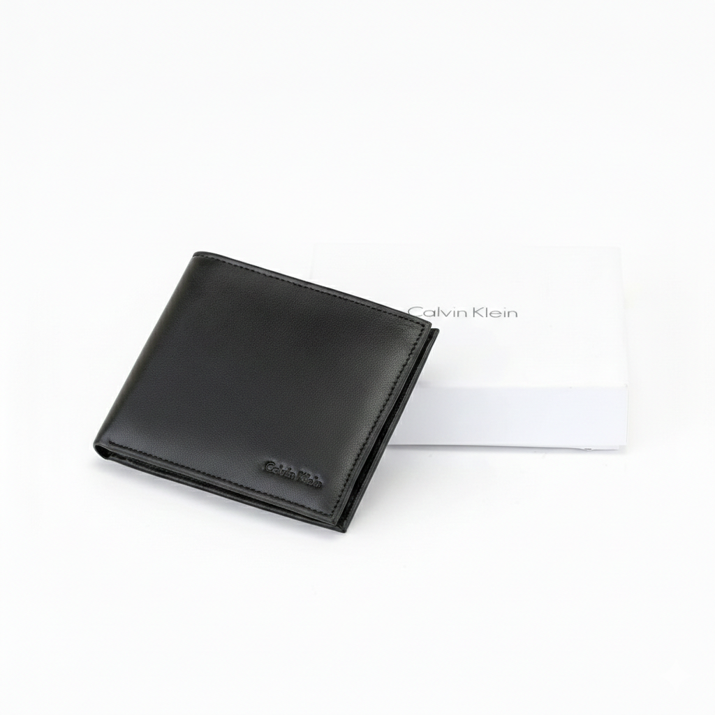 Top-down angled view of a Calvin Klein men's black smooth leather wallet with a small debossed logo, placed next to its matching closed white gift box