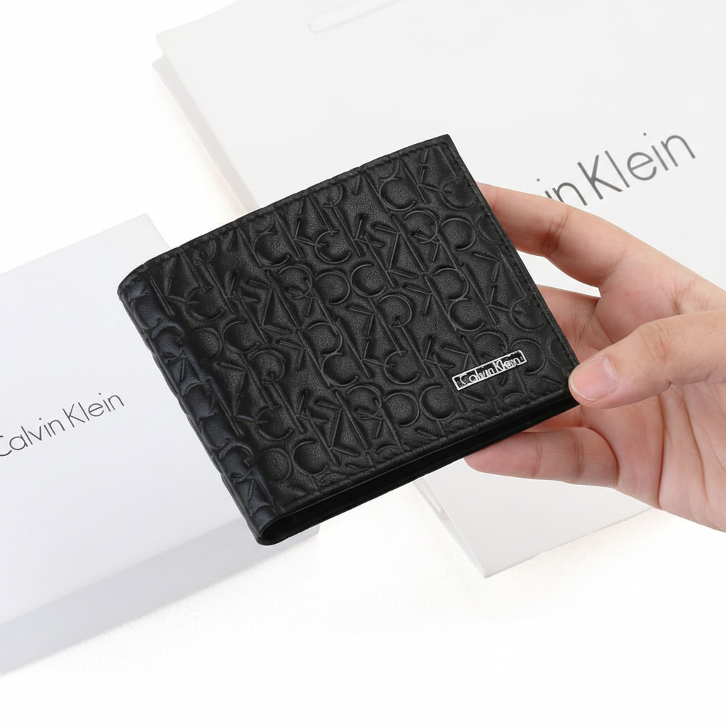 Hand holding a Calvin Klein men's black leather wallet showcasing the textured CK monogram pattern and metal plaque, presented in front of its original white branded packaging
