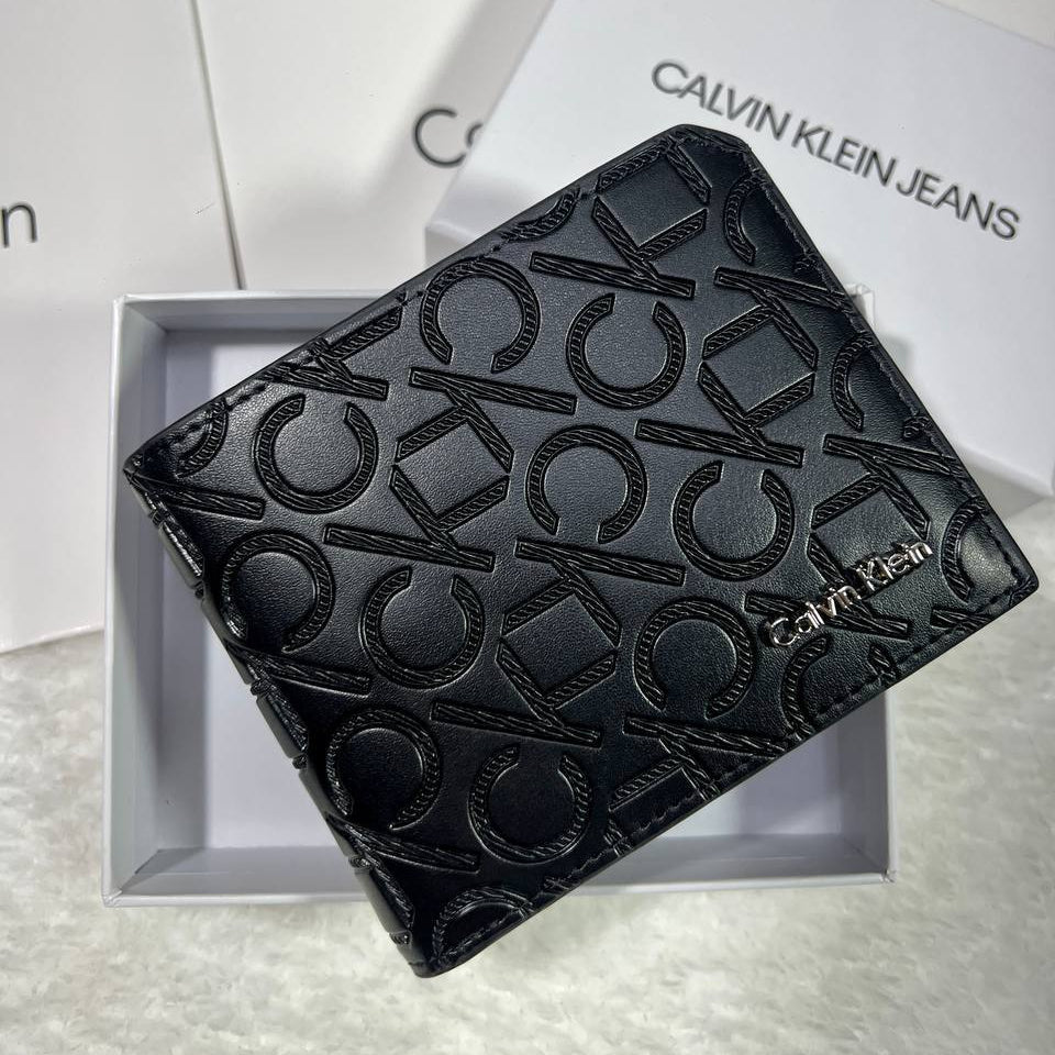 Calvin Klein men's black wallet with embossed monogram logo pattern and silver metal branding inside a white Calvin Klein Jeans gift box