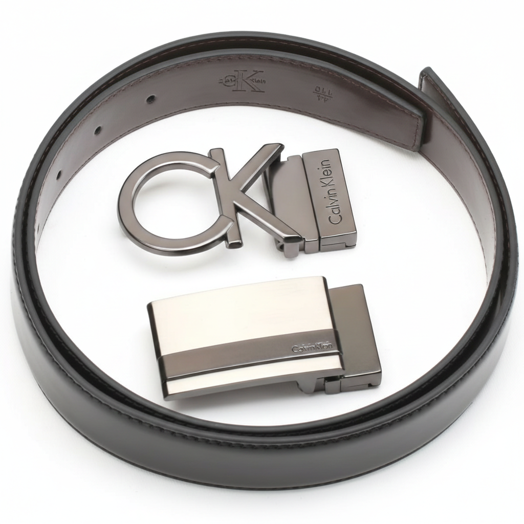 Angled perspective of a rolled Calvin Klein reversible leather belt and its two premium metal buckles, showcasing the high-quality craftsmanship and designer hardware
