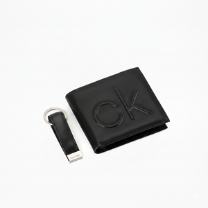 Top-down view of a premium Calvin Klein men's gift set featuring a black leather bifold wallet with a large debossed cK monogram and a matching leather keychain
