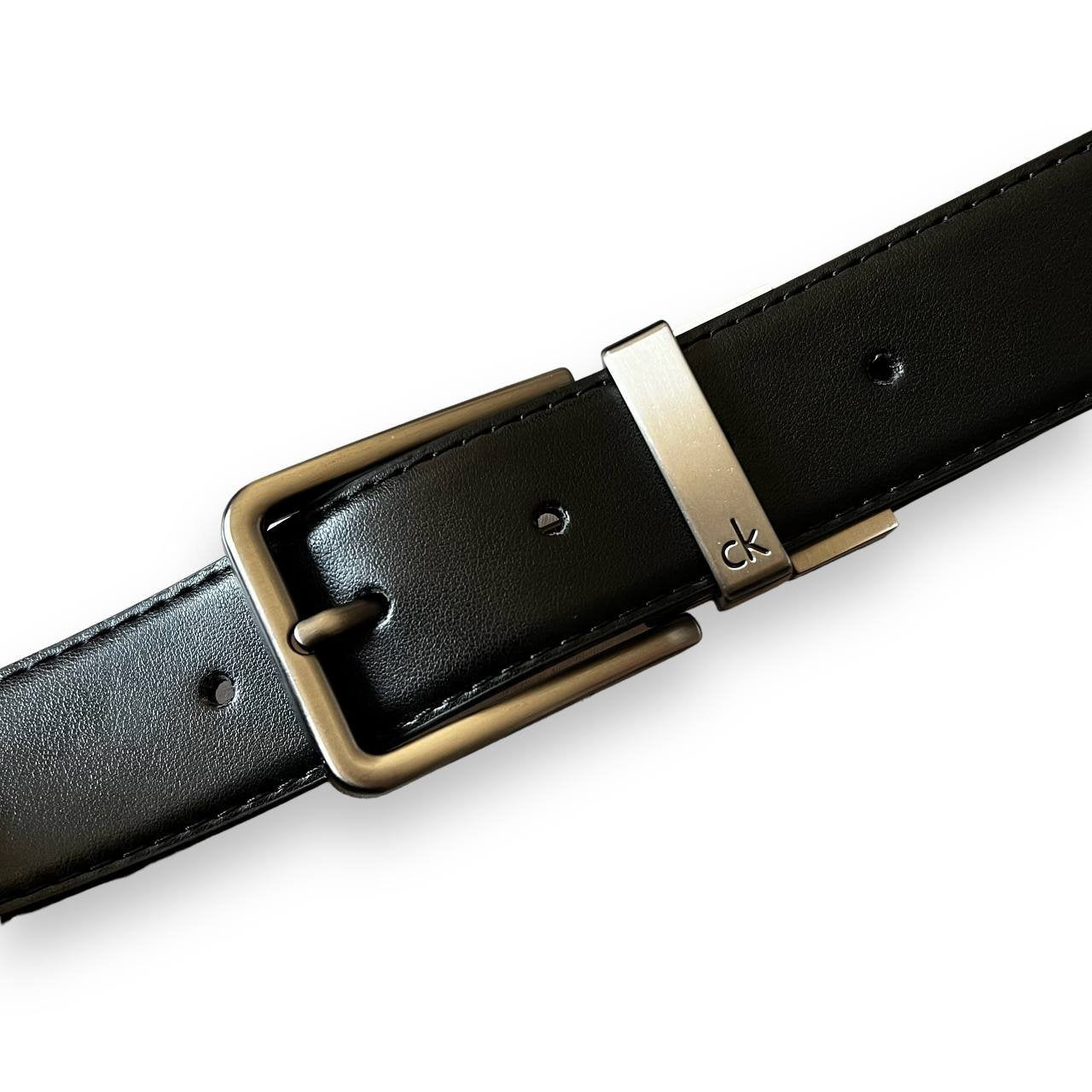 Close-up view of the gunmetal reversible belt buckle mechanism on a Calvin Klein men's leather belt.