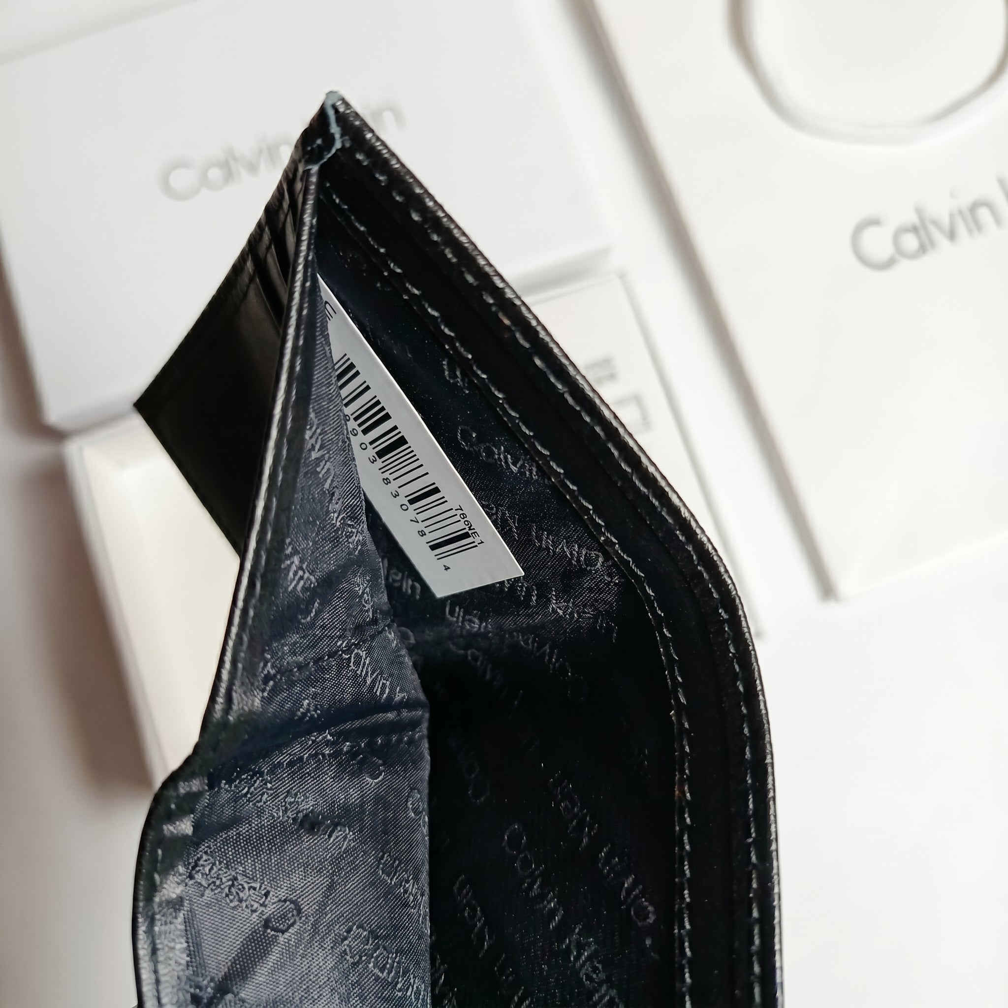 Close-up macro studio view of the Calvin Klein wallet internal compartment showing the original white tracking label and barcode tag