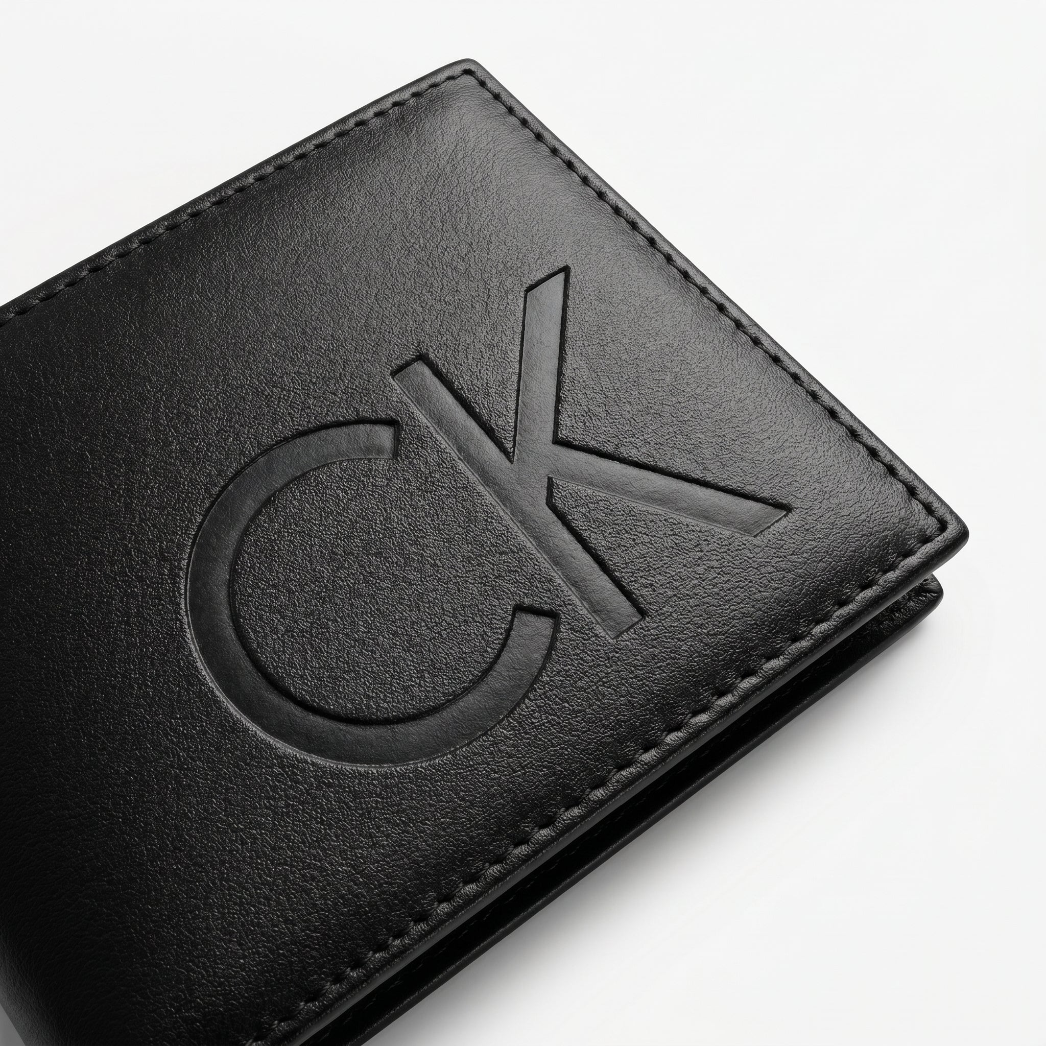 Macro close-up studio shot focusing on the large debossed CK logo over the black smooth genuine leather surface
