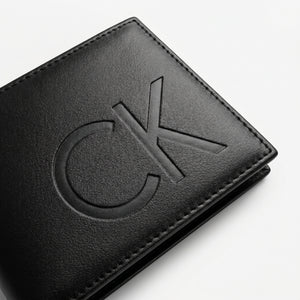 Macro close-up studio shot focusing on the large debossed CK logo over the black smooth genuine leather surface