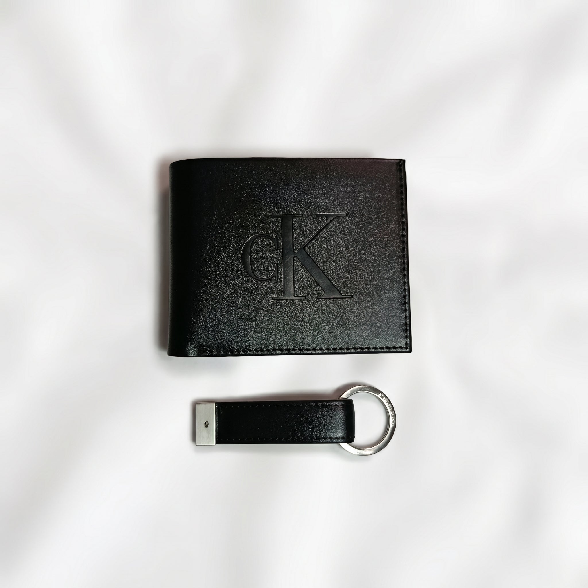 Straight studio layout view of the Calvin Klein mirror original black smooth leather wallet showing the debossed center CK logo alongside its matching standalone luxury keychain