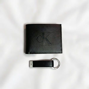 Straight studio layout view of the Calvin Klein mirror original black smooth leather wallet showing the debossed center CK logo alongside its matching standalone luxury keychain