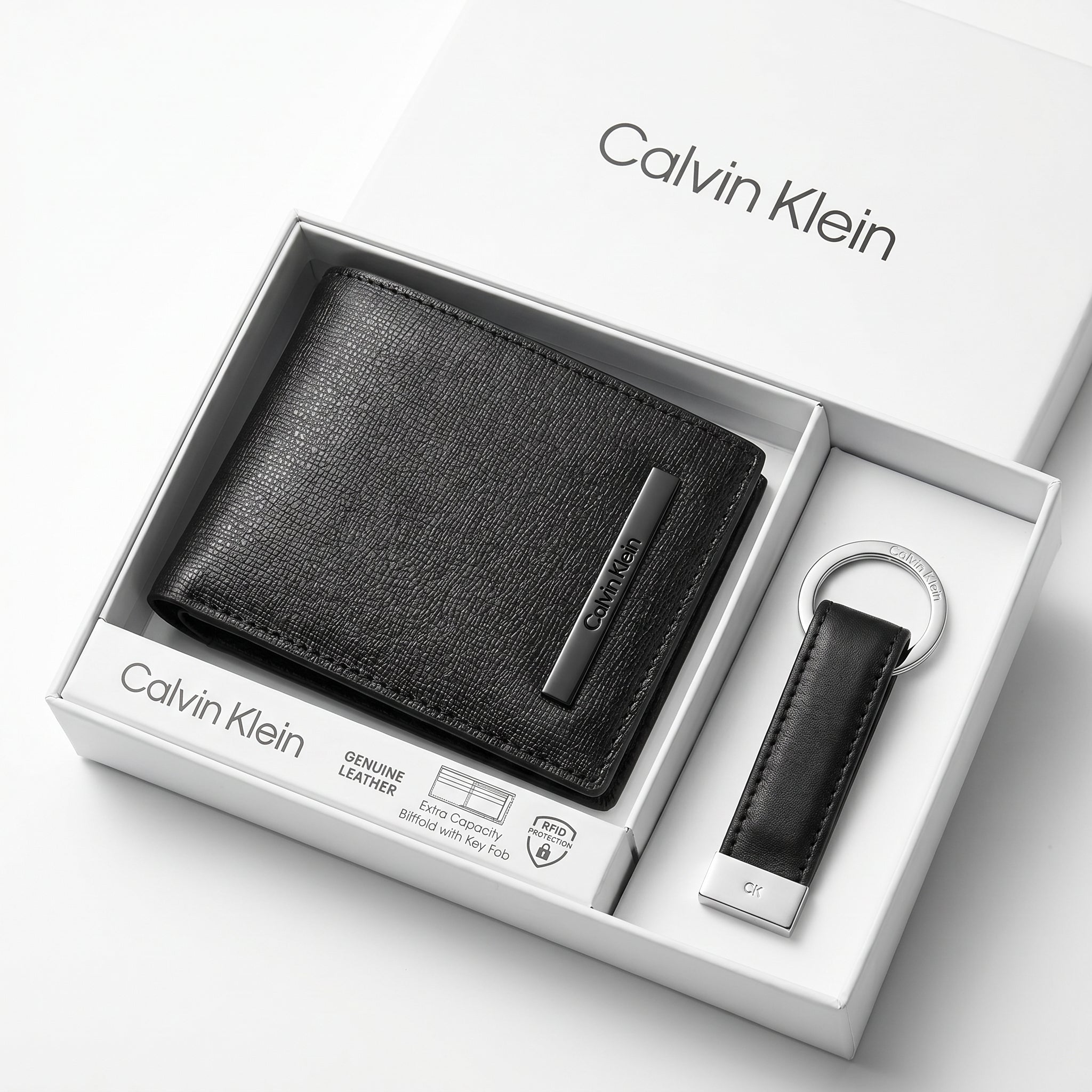 Top-down studio product photography of the Calvin Klein mirror original smooth black leather wallet and keychain set neatly resting inside its open white branded gift box