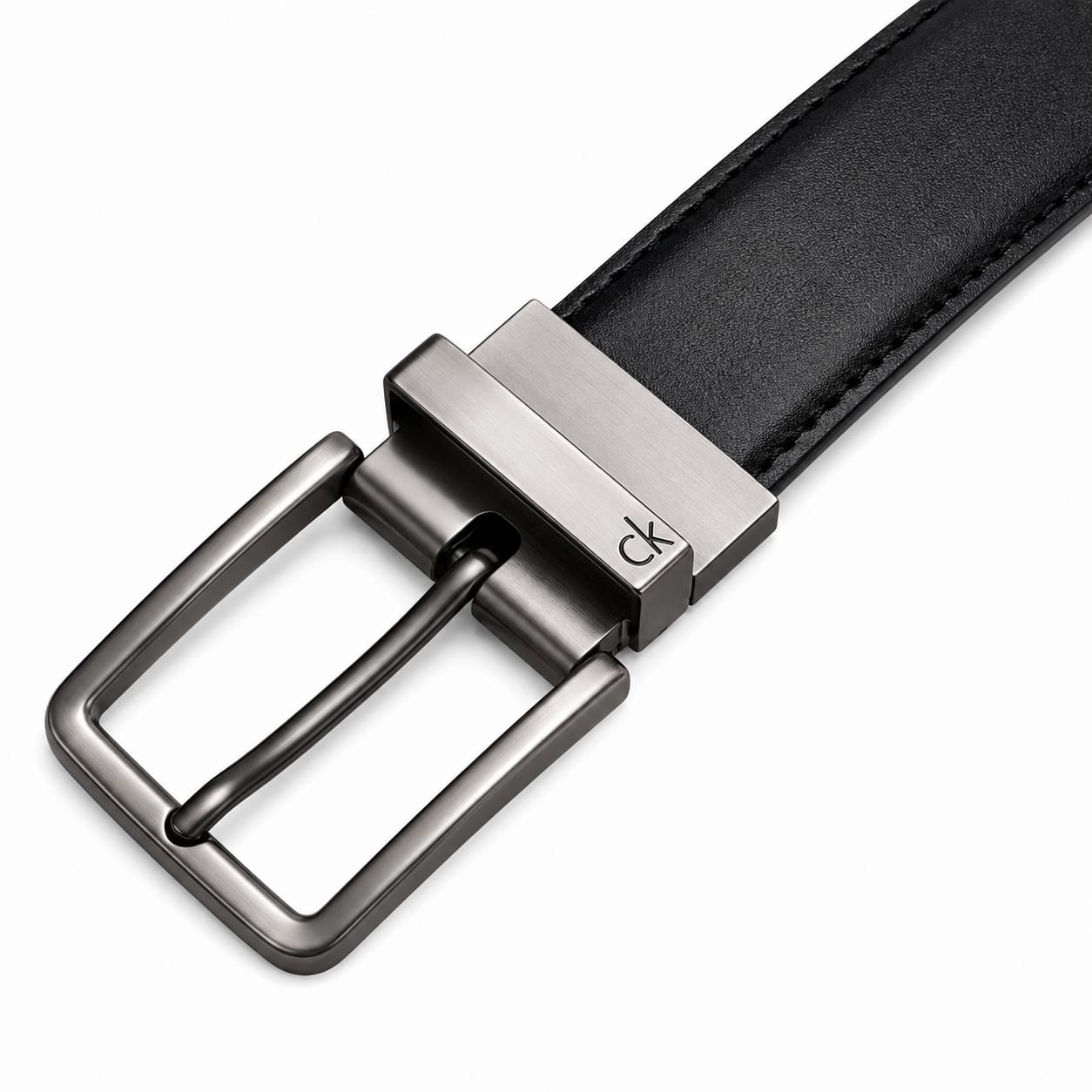 Live close-up smartphone photograph of the Calvin Klein reversible leather belt highlighting the silver rotatable buckle engraved with brand text over the black smooth side