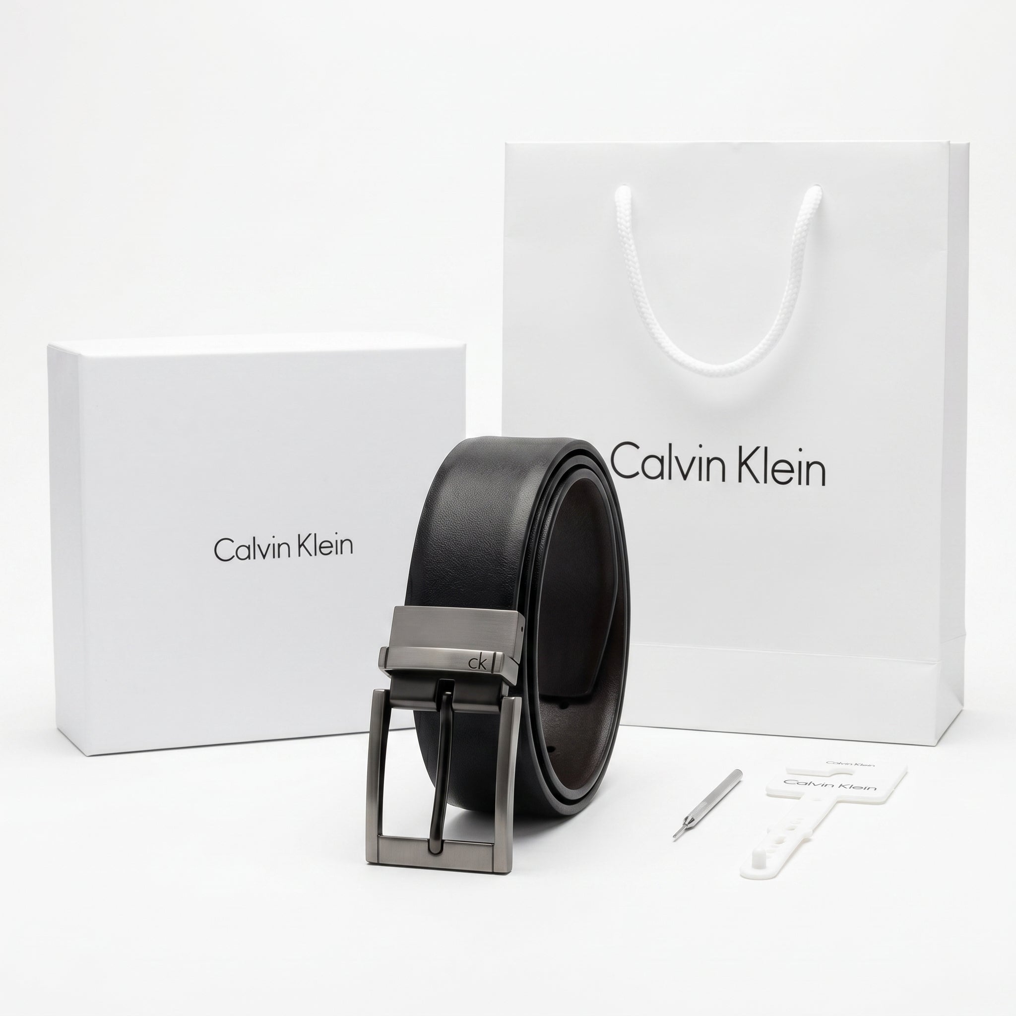 Top-down style studio product photography of the Calvin Klein mirror original reversible black leather belt neatly rolled with buckle centered