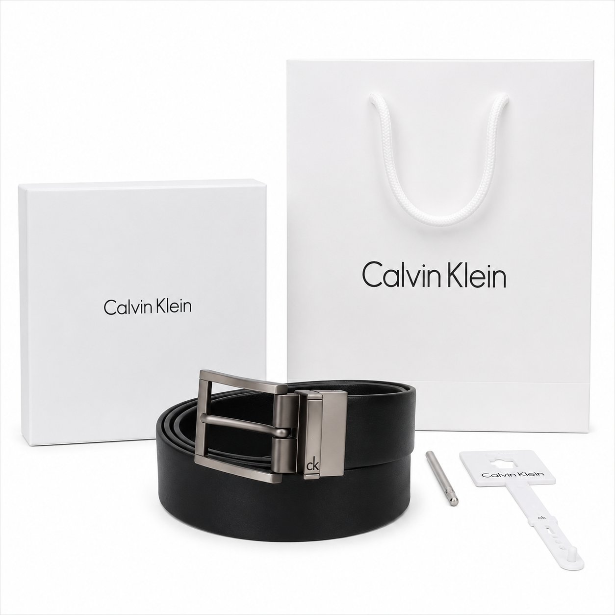 Full premium packaging presentation of the Calvin Klein mirror original reversible leather belt with its white gift box, matching shopping bag, tags, and hole punch tool