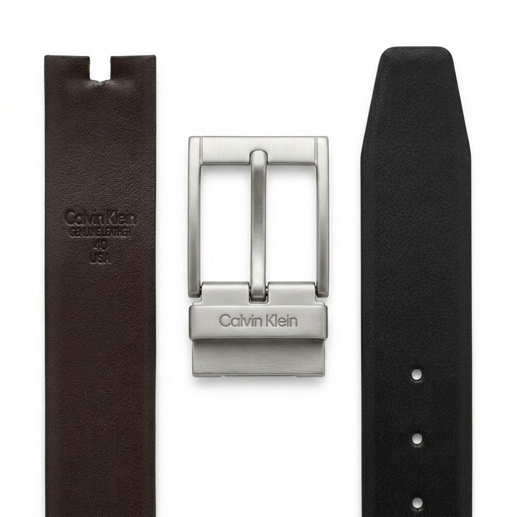 Live close-up smartphone photograph of the Calvin Klein mirror original reversible belt highlighting the disassembled gunmetal buckle with vertical logo alongside the brown leather side with embossed brand stamp