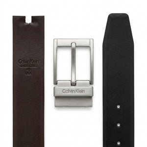 Live close-up smartphone photograph of the Calvin Klein mirror original reversible belt highlighting the disassembled gunmetal buckle with vertical logo alongside the brown leather side with embossed brand stamp