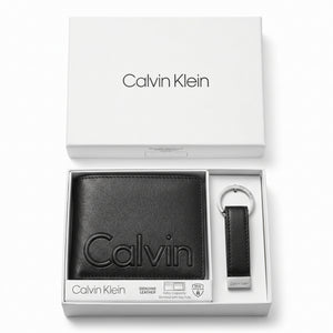 Top-down studio product photography of the Calvin Klein mirror original smooth black leather wallet and matching keychain set neatly arranged inside its open white branded gift box