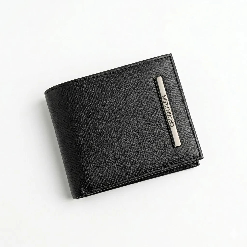 Macro close-up studio shot focusing on the engraved silver metal Calvin Klein logo plate over the black smooth genuine leather surface