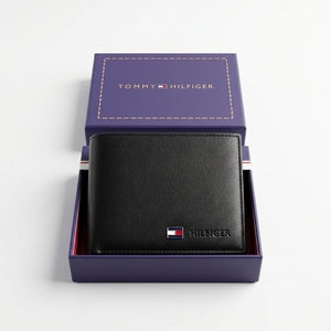 Top-down studio photograph of the Tommy Hilfiger smooth black leather wallet neatly placed inside its open premium navy gift box