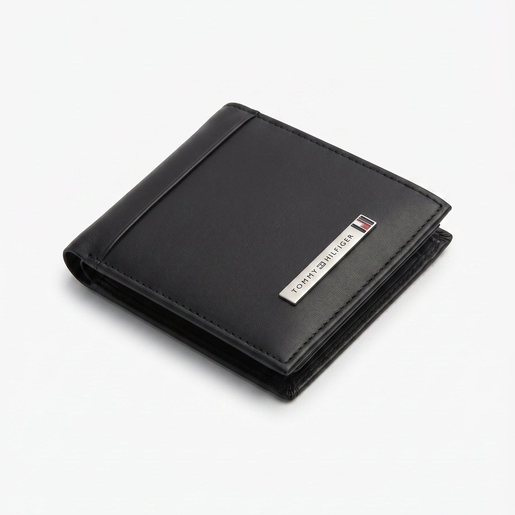 Close-up perspective shot focusing on the engraved Tommy Hilfiger silver metal bar logo and fine stitching on smooth leather