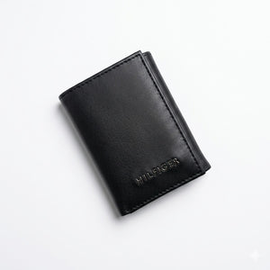 Professional angled studio photograph of the sleek Tommy Hilfiger mirror original smooth black leather trifold wallet