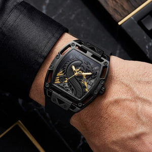 A close-up of a GUESS wristwatch with a black skeletonized case and dragon dial, worn on a person's wrist against a dark marble background.