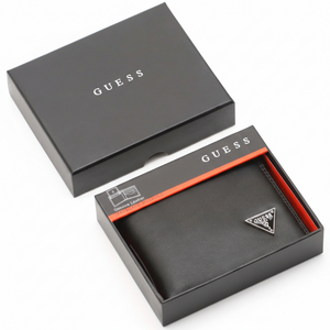 A Guess men's black smooth leather bifold wallet with a silver metal triangle logo, placed elegantly next to its matching closed black gift box