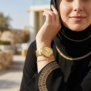 Half-face lifestyle shot of a woman with fair skin wearing bracelets and rings on the same hand as the Guess Montauk gold metal watch for a sophisticated everyday look
