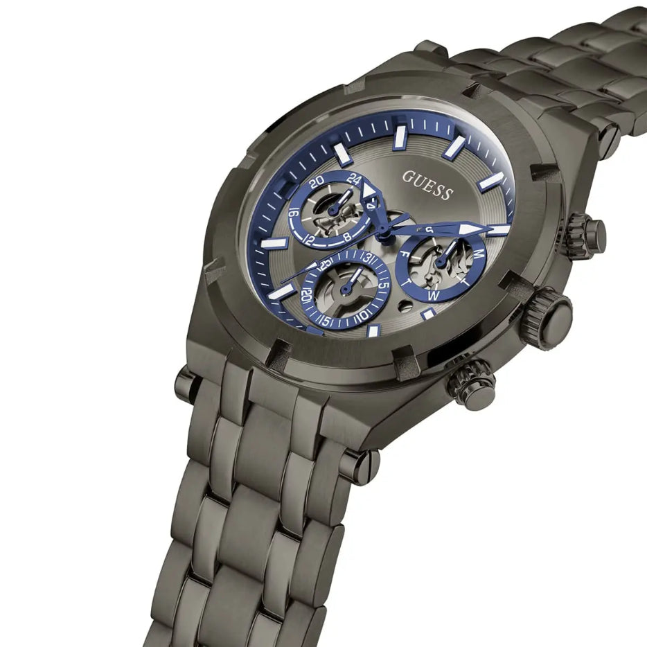 A GUESS men's chronograph watch featuring a dark gunmetal gray stainless steel case and link bracelet, with a blue dial and three sub-dials.