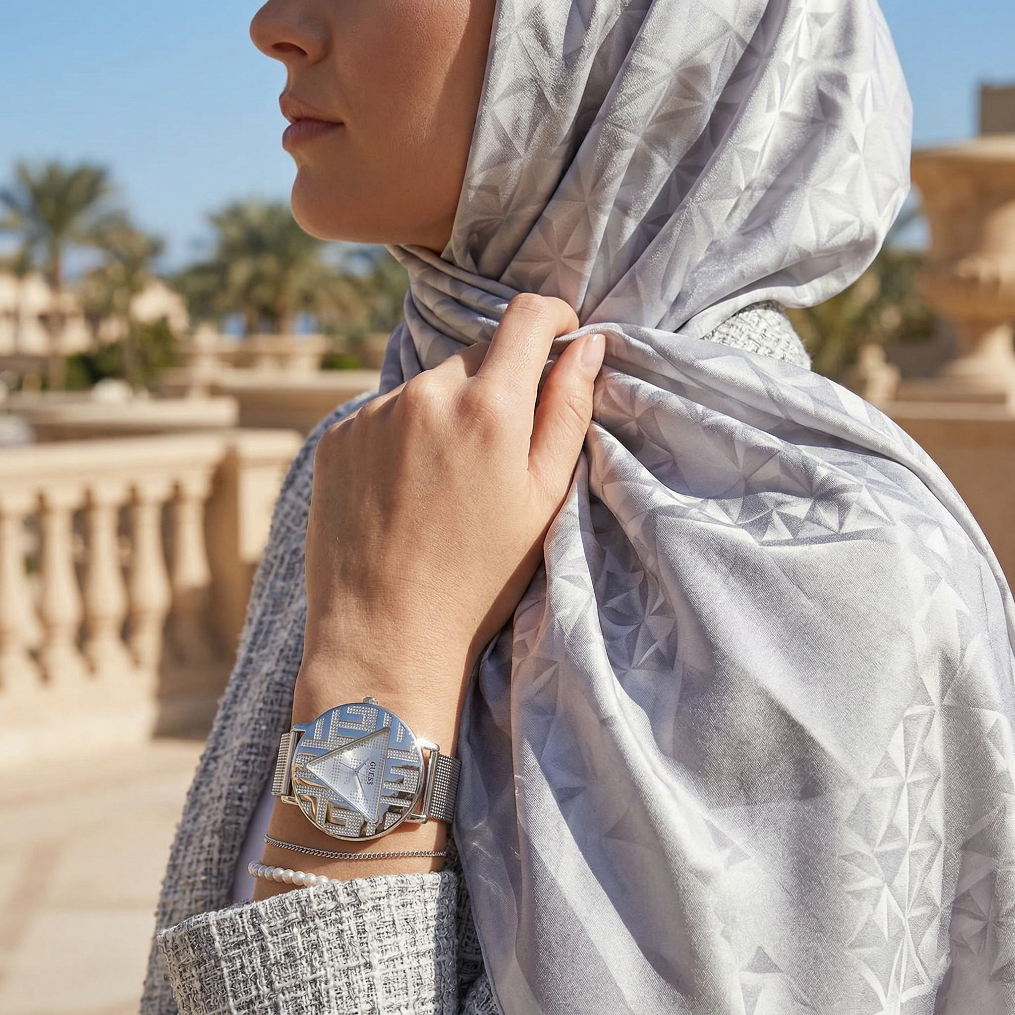Elegant woman wearing Guess Iconic GW0527L1 women's quartz battery watch with silver case and luxury silver mesh bracelet