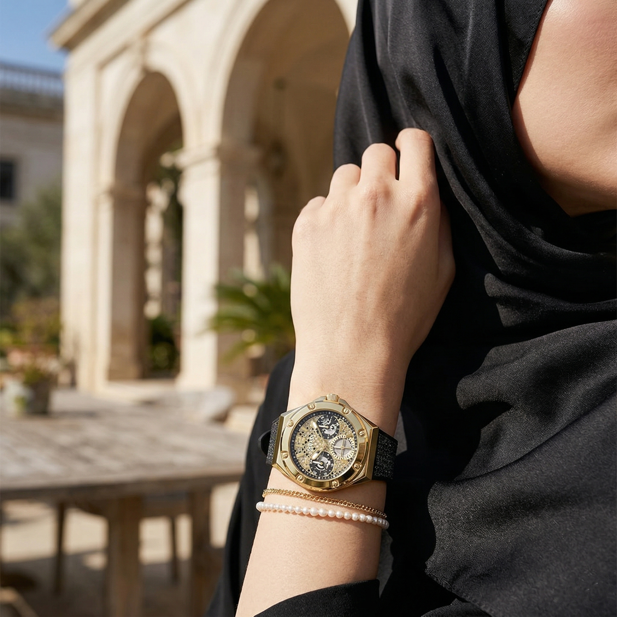 Elegant woman wearing Guess Asteria GW0620L2 women's quartz battery watch with gold case and luxury black rubber strap