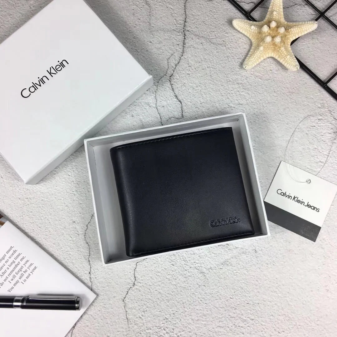 Hand holding a Calvin Klein men's black full grain leather wallet featuring a matte vertical stripe and small debossed logo, displayed above an open white gift box and shopping bag