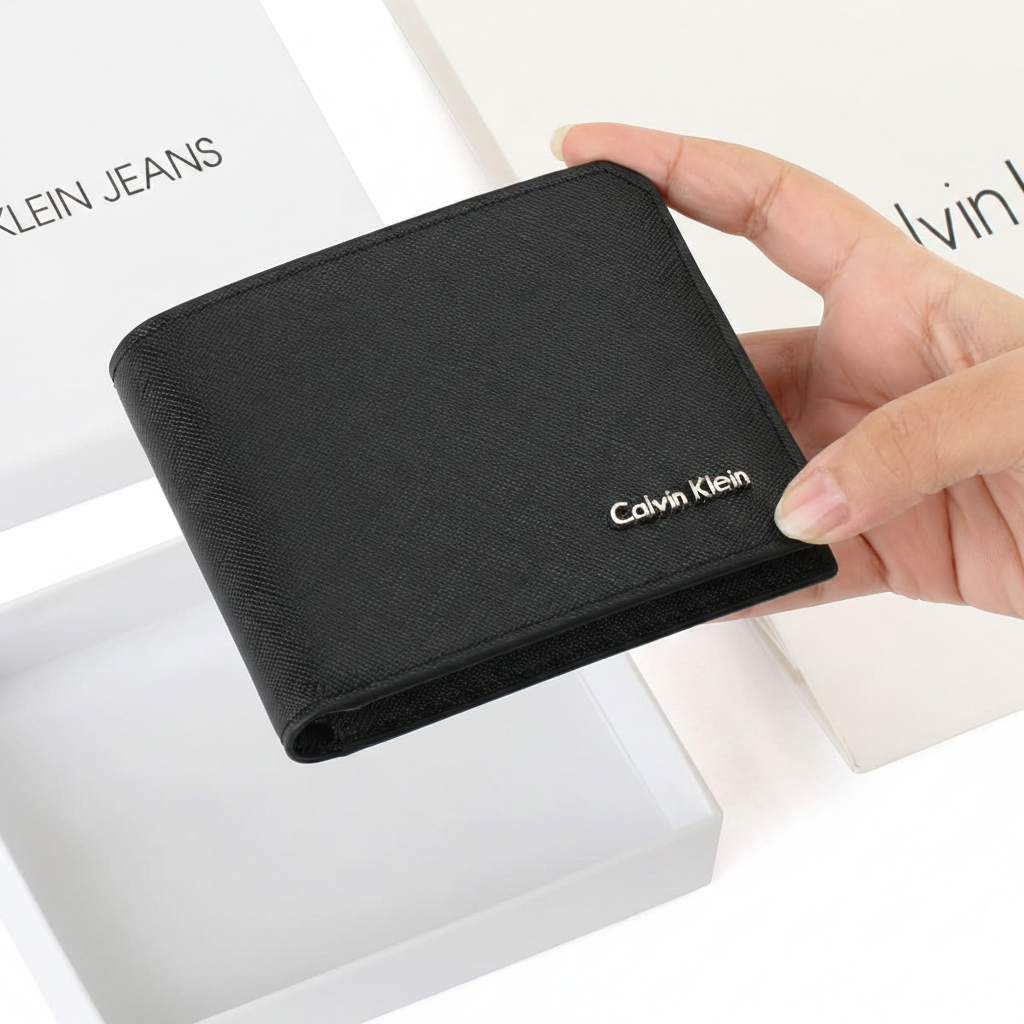Hand holding a closed Calvin Klein men's black saffiano leather wallet featuring a silver metal logo, displayed above its original open white branded gift box
