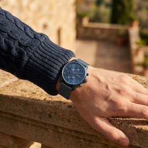 Half-face lifestyle shot of a man with fair skin wearing bracelets on the same hand as the Hugo Boss Skymaster blue mesh watch for a sophisticated everyday look