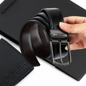 Hand holding a rolled Hugo Boss black leather belt with a classic buckle, displayed in front of an official branded gift bag