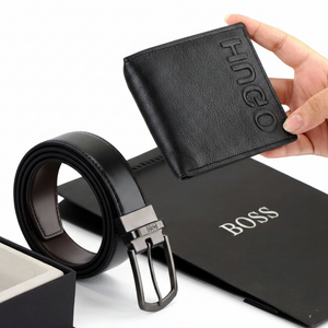Hand holding a rolled Hugo Boss black leather belt with a classic buckle, displayed in front of an official branded gift bag