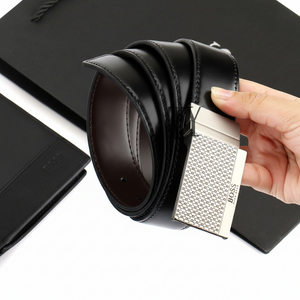 Hand holding a rolled Hugo Boss black leather belt featuring a modern textured metal buckle against a dark background