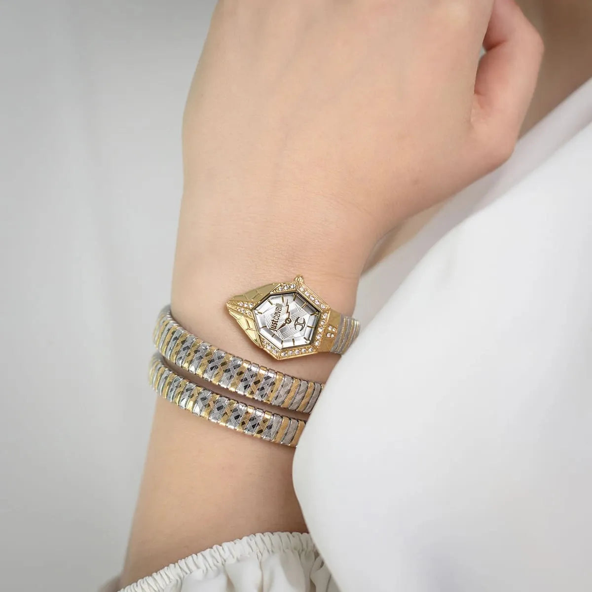 Gold watch and bracelet on a wrist against a neutral background