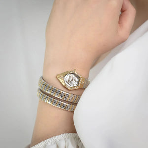 Gold watch and bracelet on a wrist against a neutral background