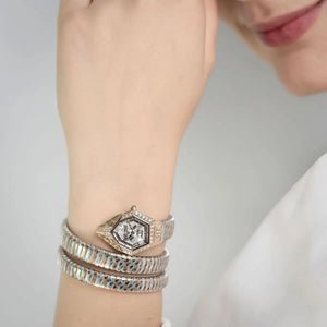 Close-up of a wrist wearing multiple silver bracelets with a neutral background