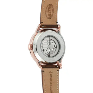 Fossil automatic watch shown from the back, featuring a tan leather strap and a rose gold case with a transparent crystal back revealing the mechanical movement.