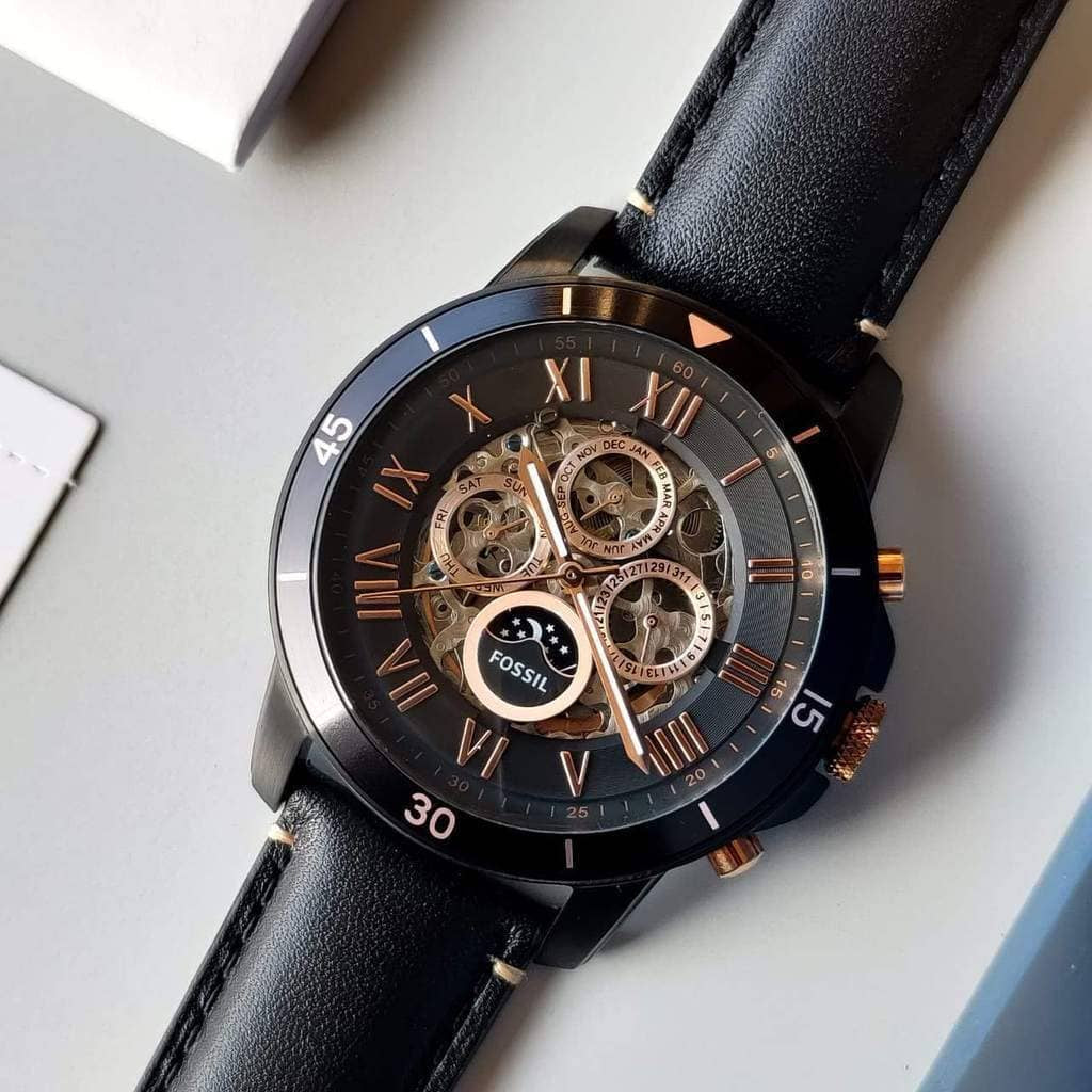 Black wristwatch with a detailed face on a light gray surface