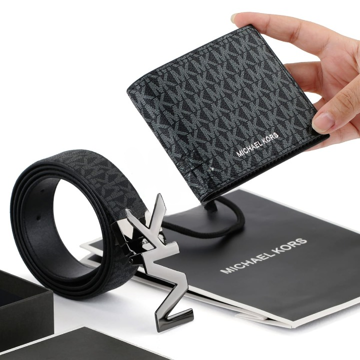 Hand holding a Michael Kors men's black monogram wallet above a reversible belt, MK buckle, and black branded gift bag