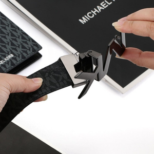 Hands demonstrating the rotating mechanism of a dark metal MK buckle on a Michael Kors men's reversible monogram belt