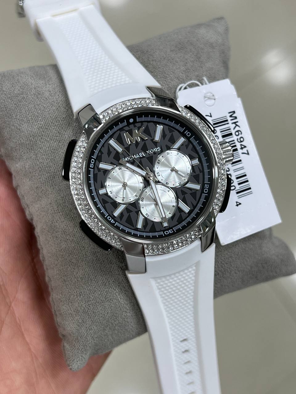Close-up of the silver-tone Michael Kors branding and luminous hands on the black Sidney MK6947 dial