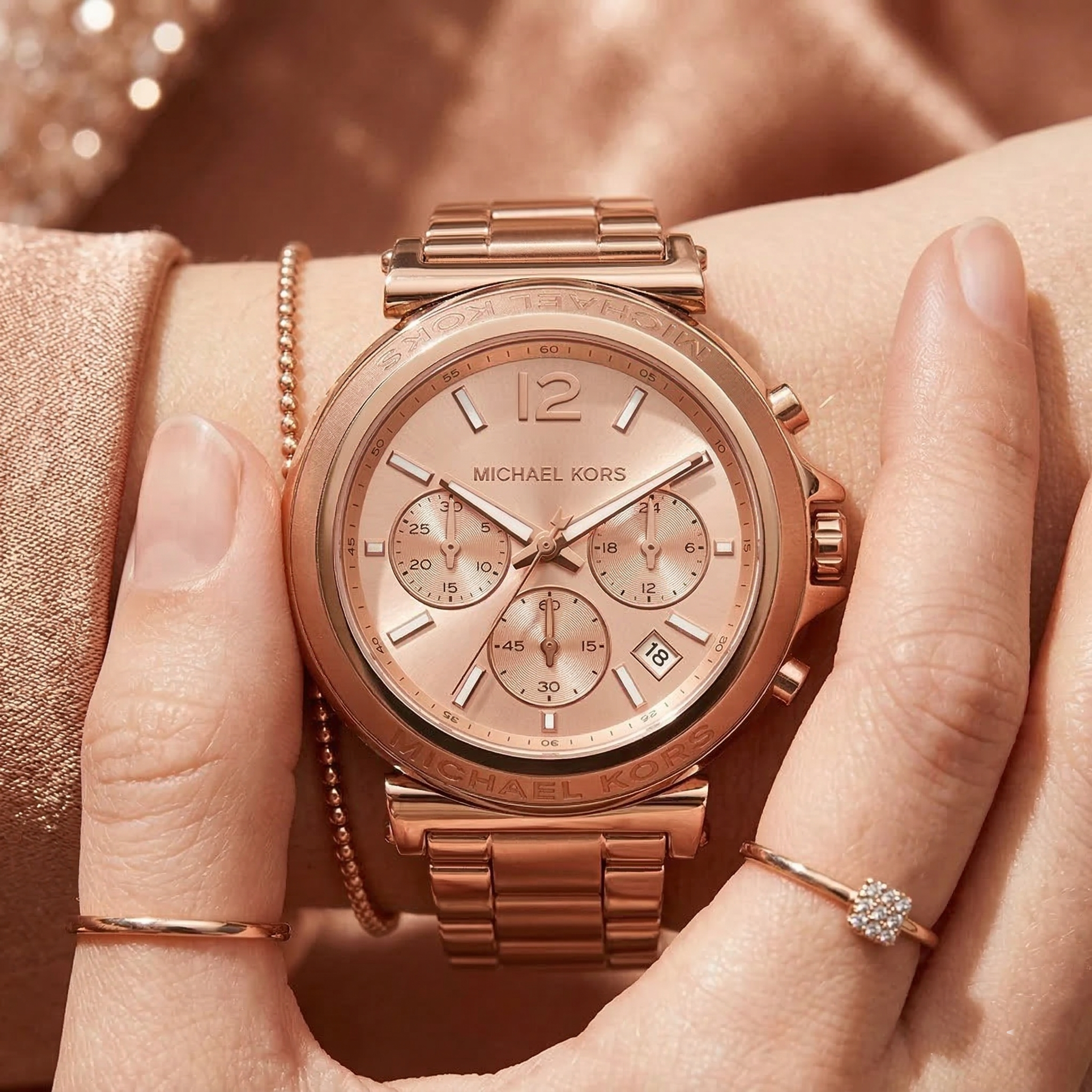 Close up of Michael Kors Raquel MK4688 women's quartz battery watch on wrist showing rose gold sunray dial and faceted metal case