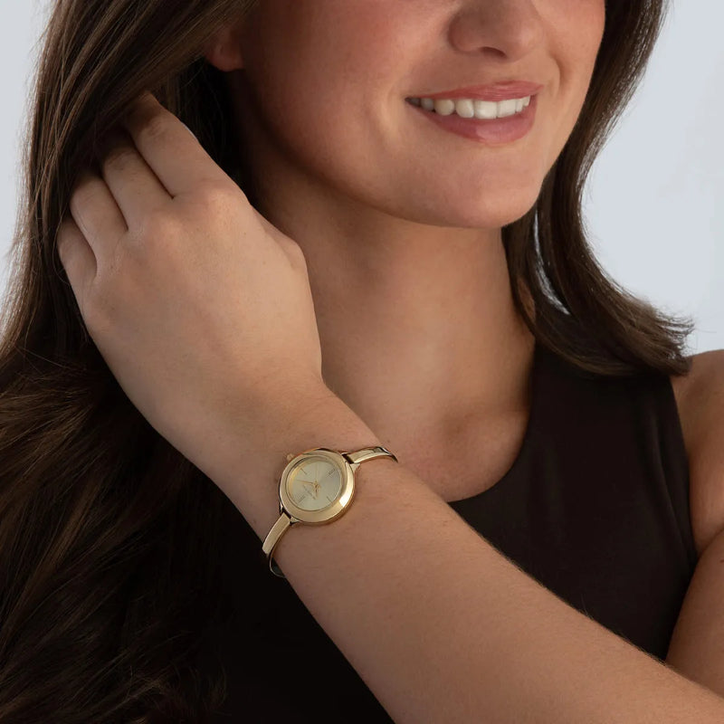 Woman wearing a gold watch on her wrist with a plain background