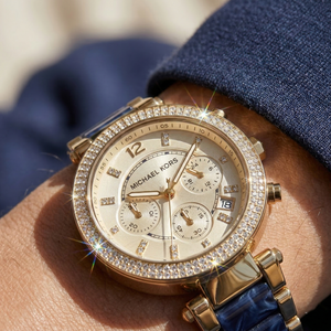 Close up of Michael Kors Parker MK6238 women's quartz battery watch on wrist showing champagne sunray dial and navy blue acetate link bracelet