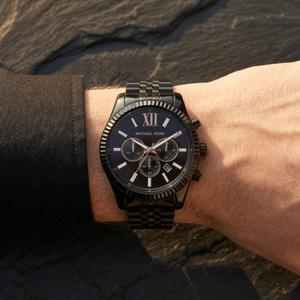 Close up of Michael Kors Lexington MK8467 men's quartz battery watch on wrist showing black sunray dial and black metal bracelet