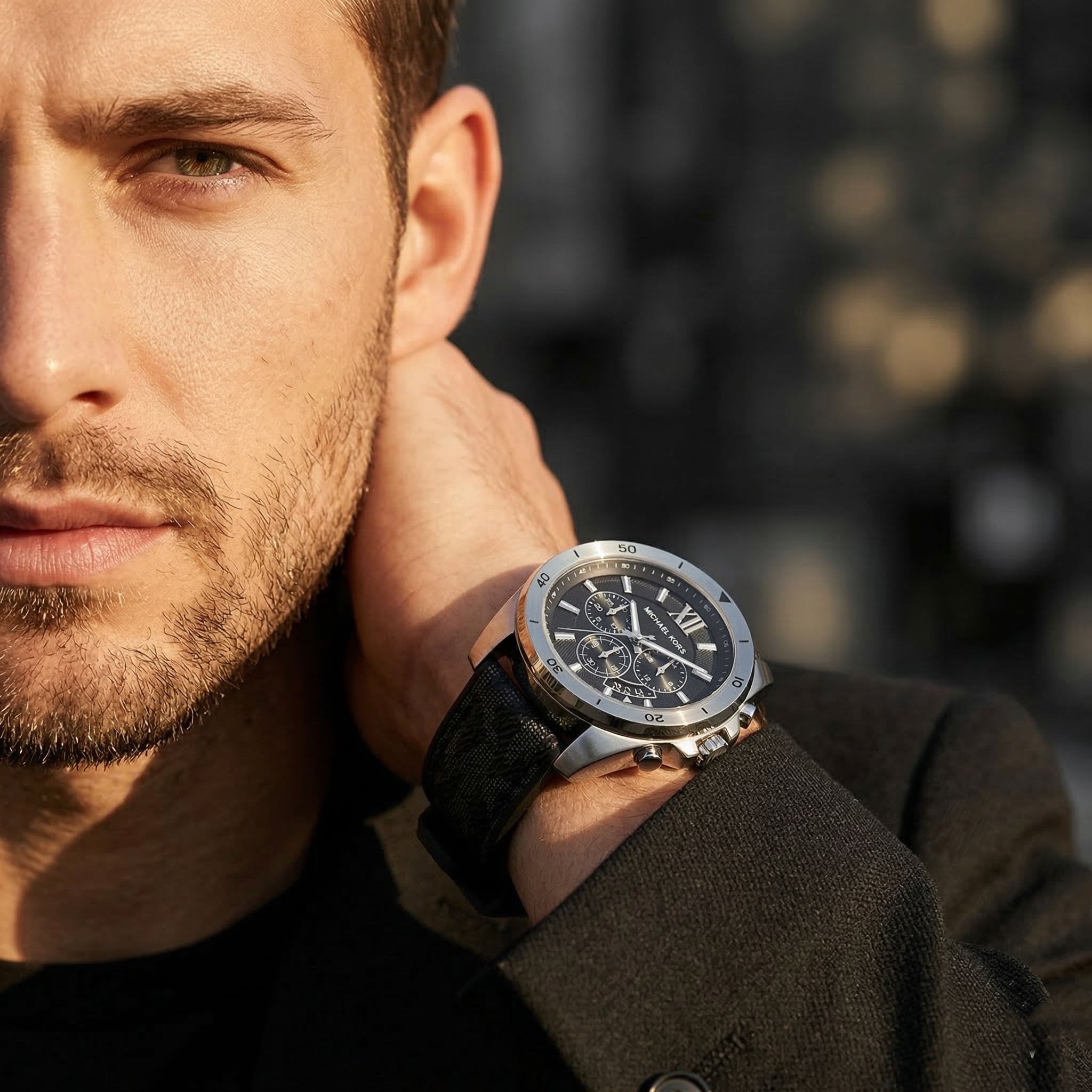 Elegant man wearing Michael Kors Brecken MK8850 men's quartz battery watch with silver-tone case and black logo rubber strap